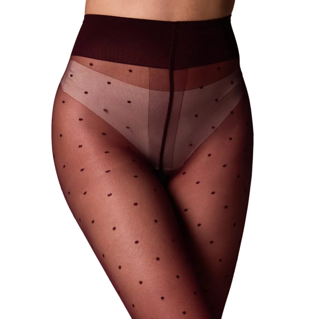 A close-up of a model's lower torso and legs wearing sheer black polka-dot tights with a wide dark waistband over a white background.