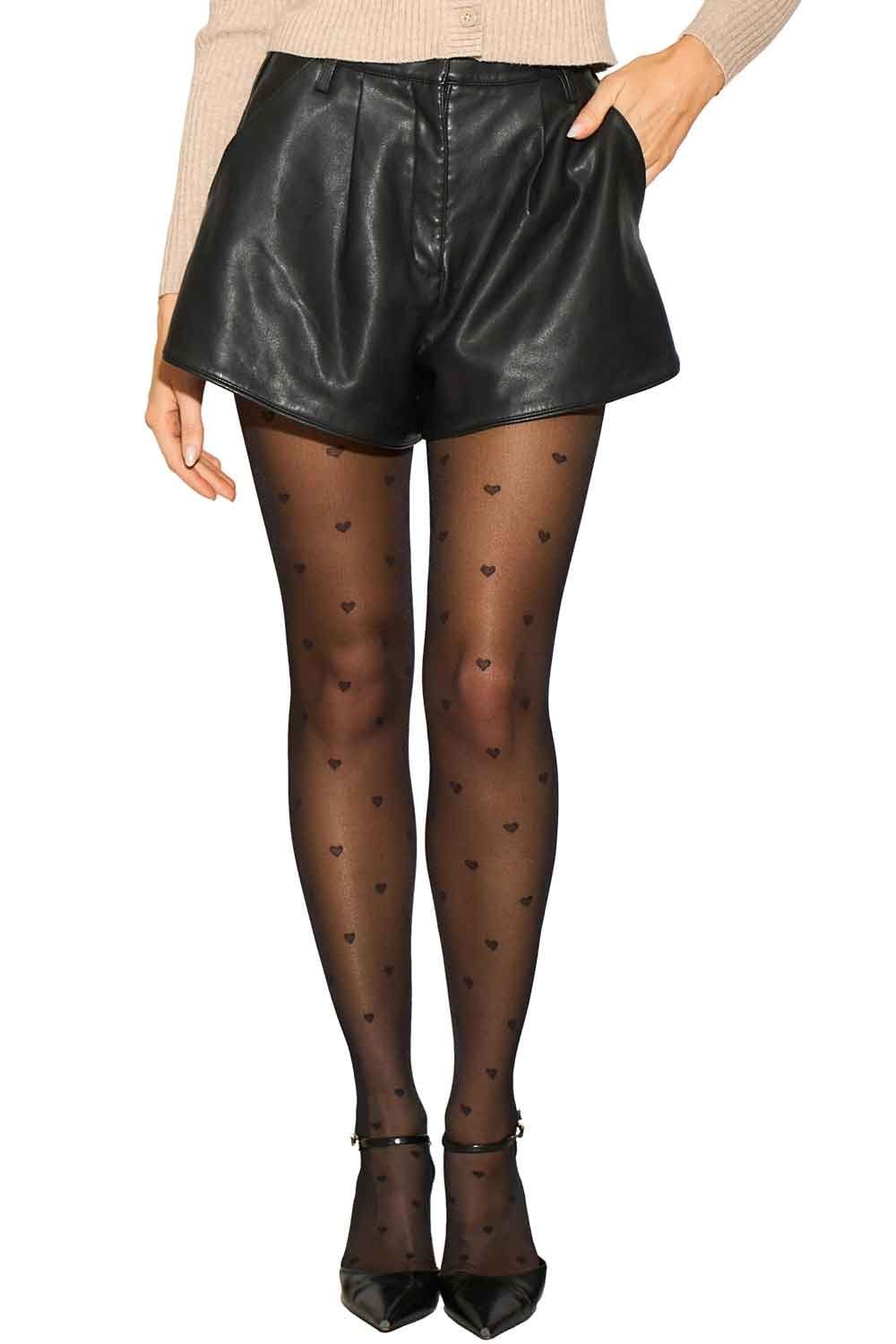 Model wearing black leather shorts and heart-patterned tights on a white background