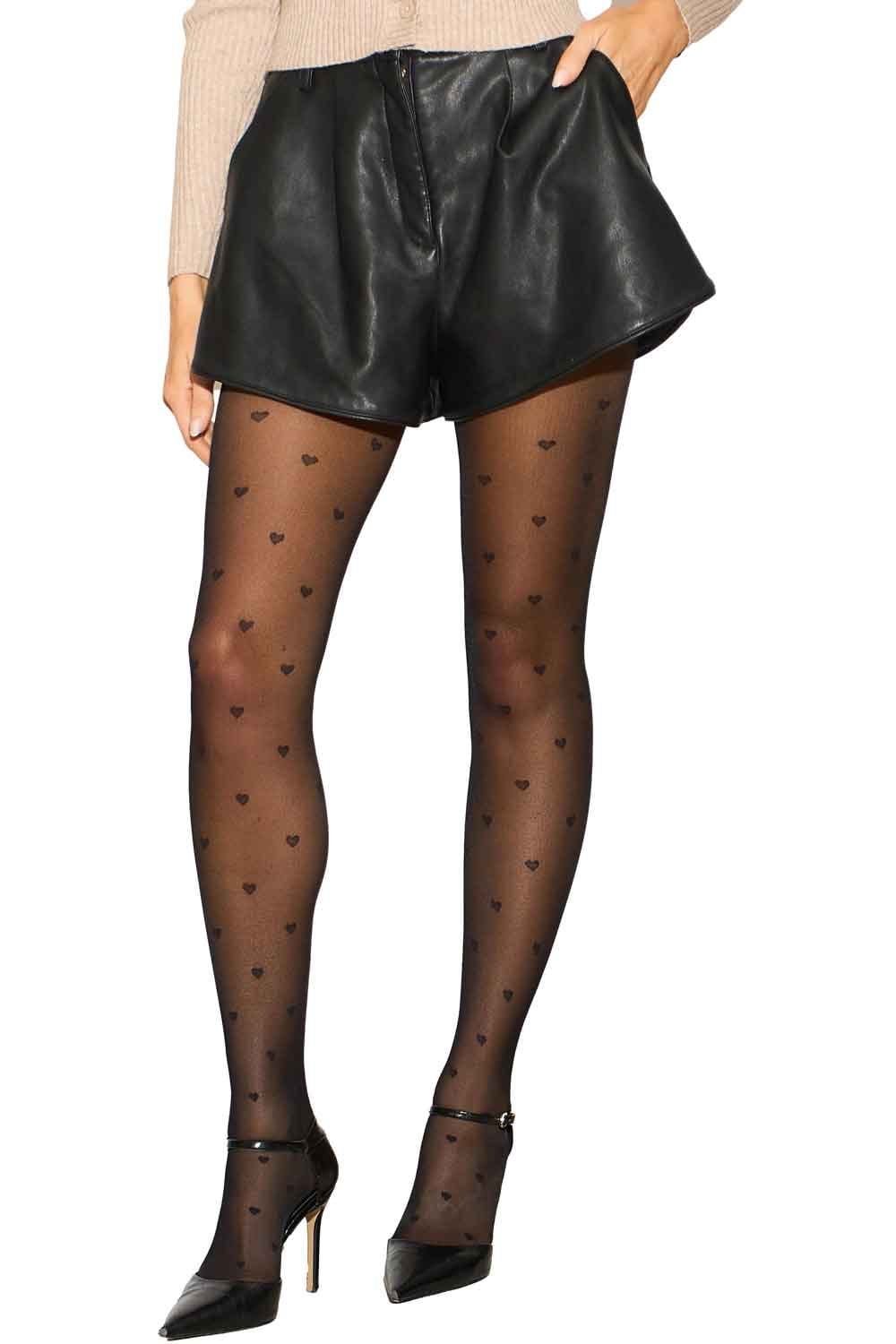 Model wearing black leather shorts and heart-patterned tights on a white background