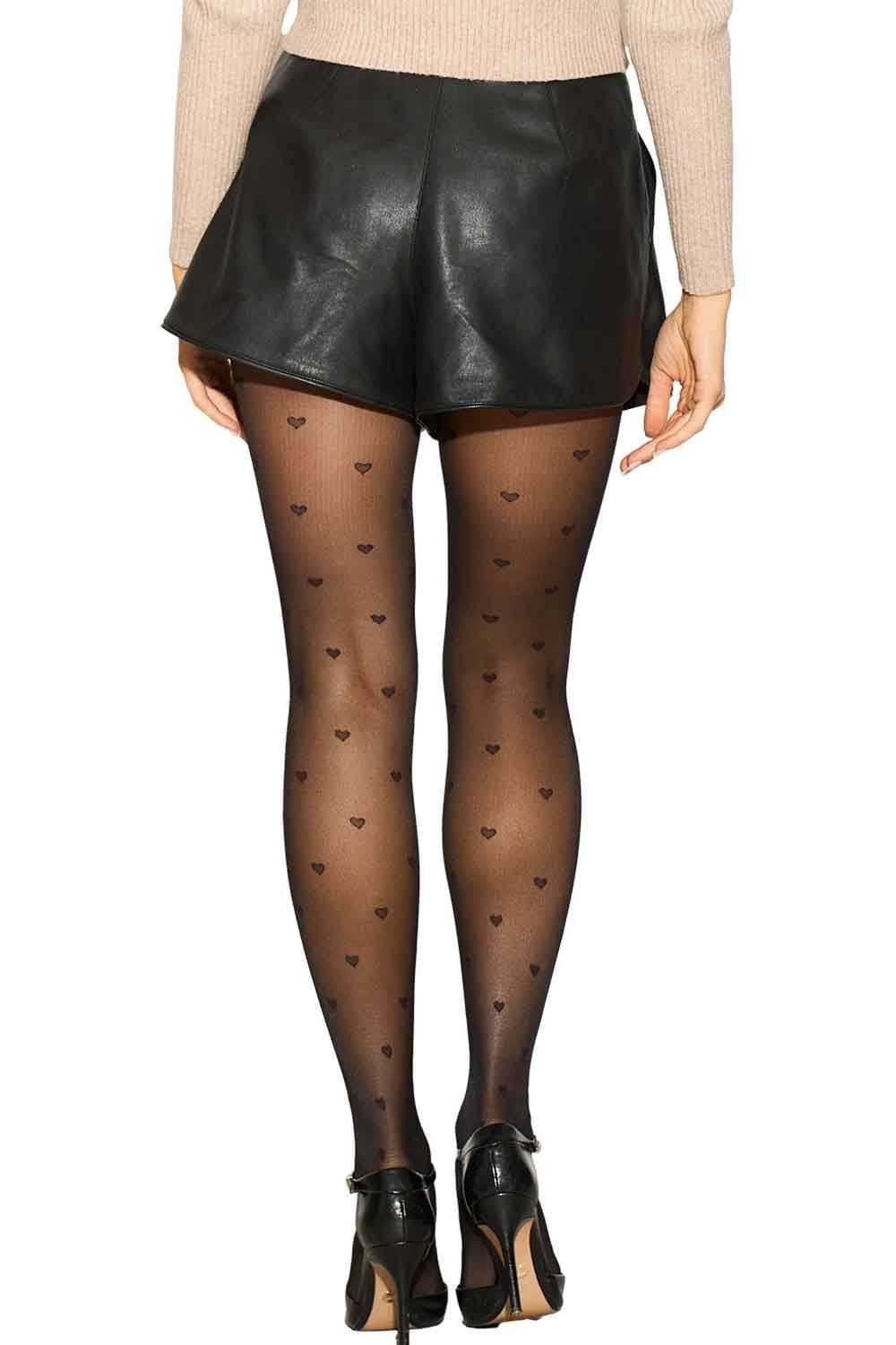Model wearing black leather shorts and heart-patterned tights on a white background