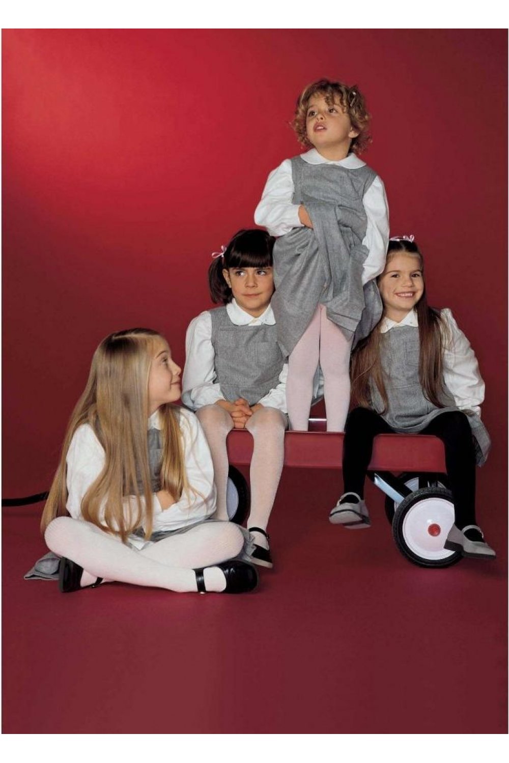 Children in matching outfits and tights posing against a red background 