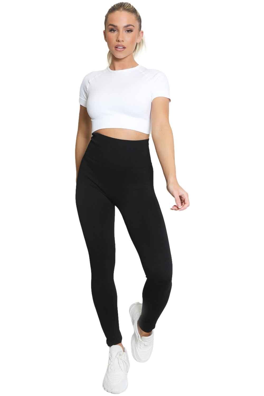 Model  wearing black leggings and a white crop top on a white background