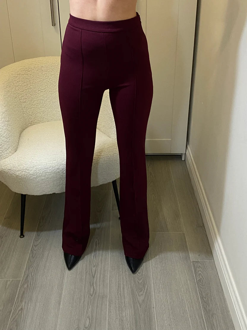 Flared tailored burgundy trousers by Allana, model standing in front of a chair