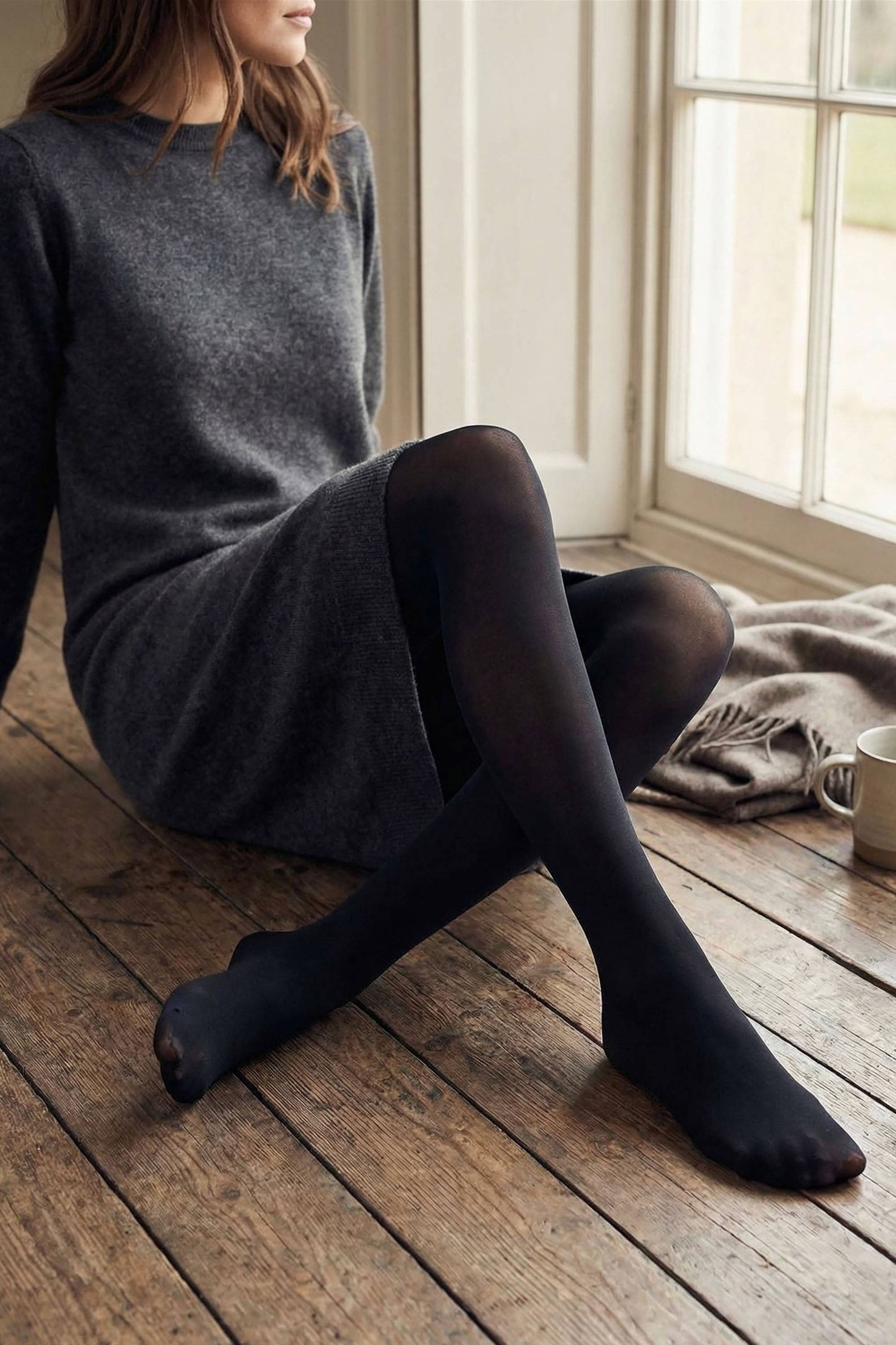 Model sitting on the floor wear a grey jumper dress and black tights
