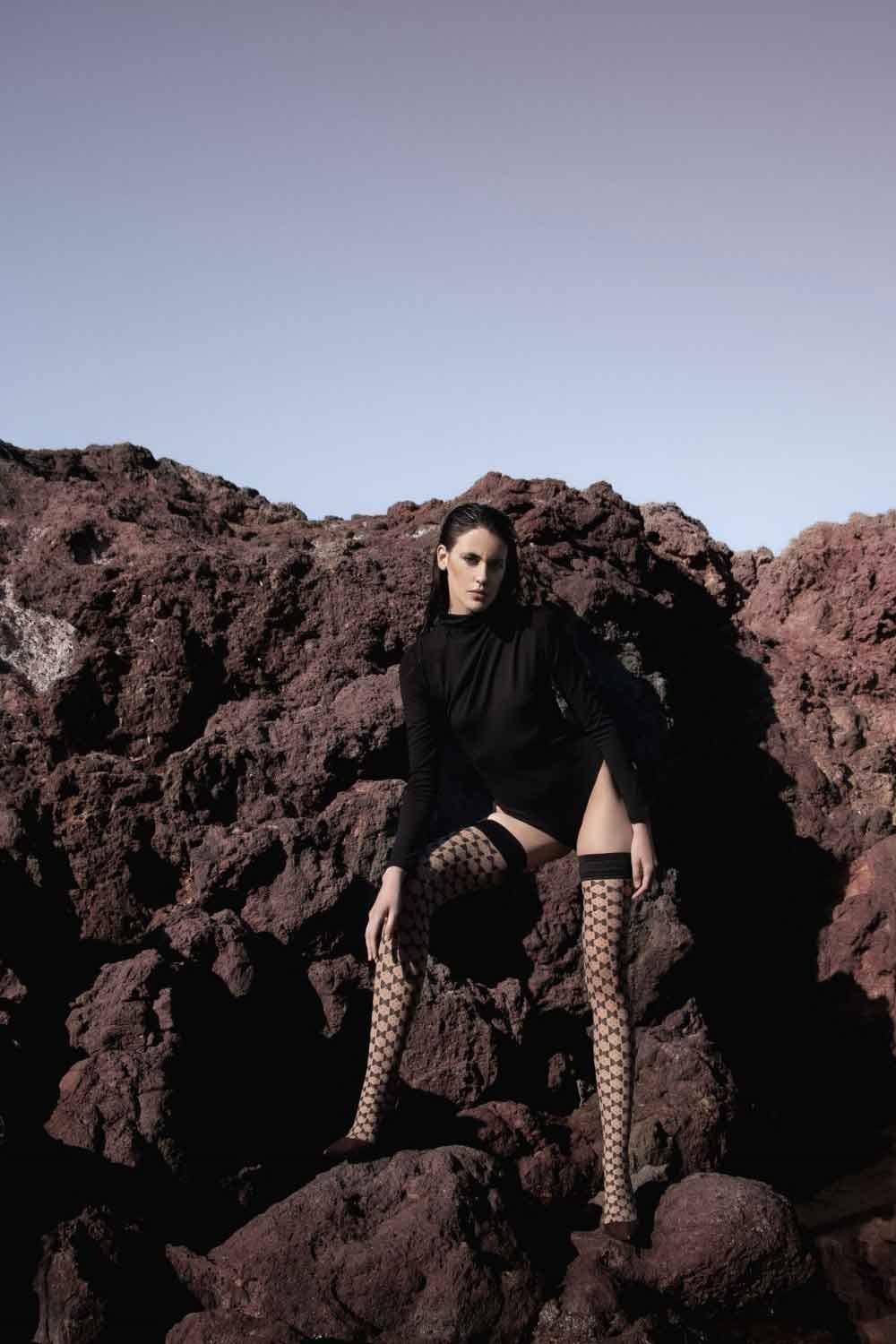 Person in black outfit and patterned Bellatrix hold ups sitting on rocky terrain