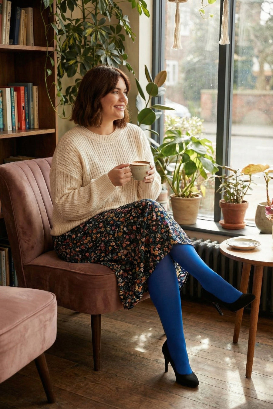 Woman sitting on a pink chair wearing a jumper, skirt and blue tights