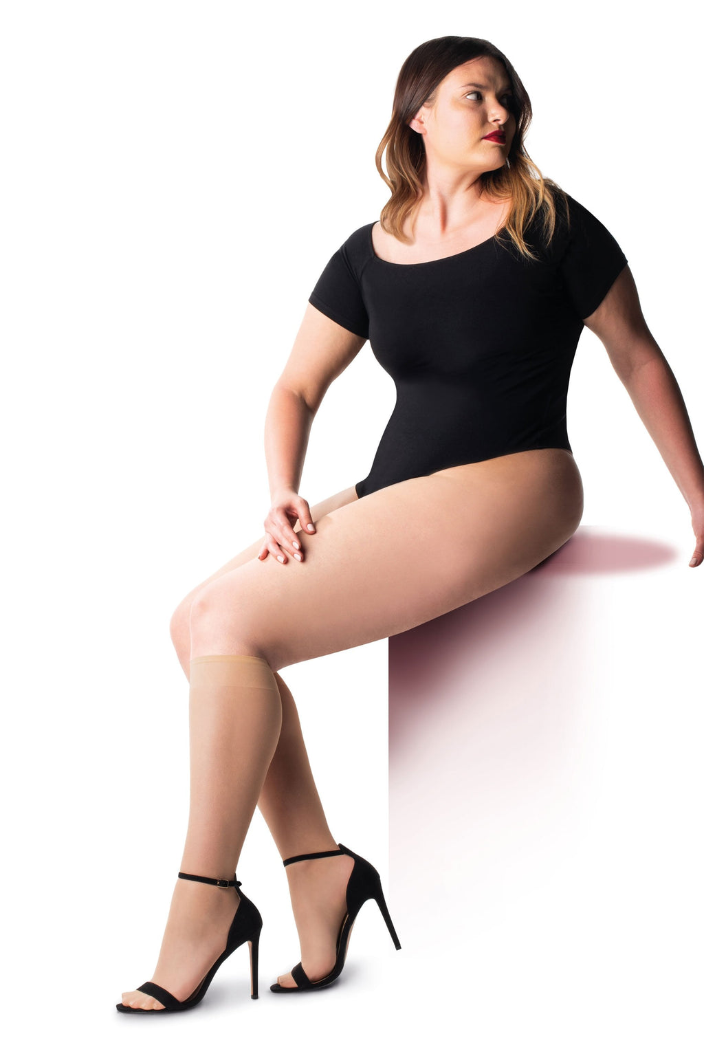 Woman wearing a black bodysuit and nude knee highs on a white background