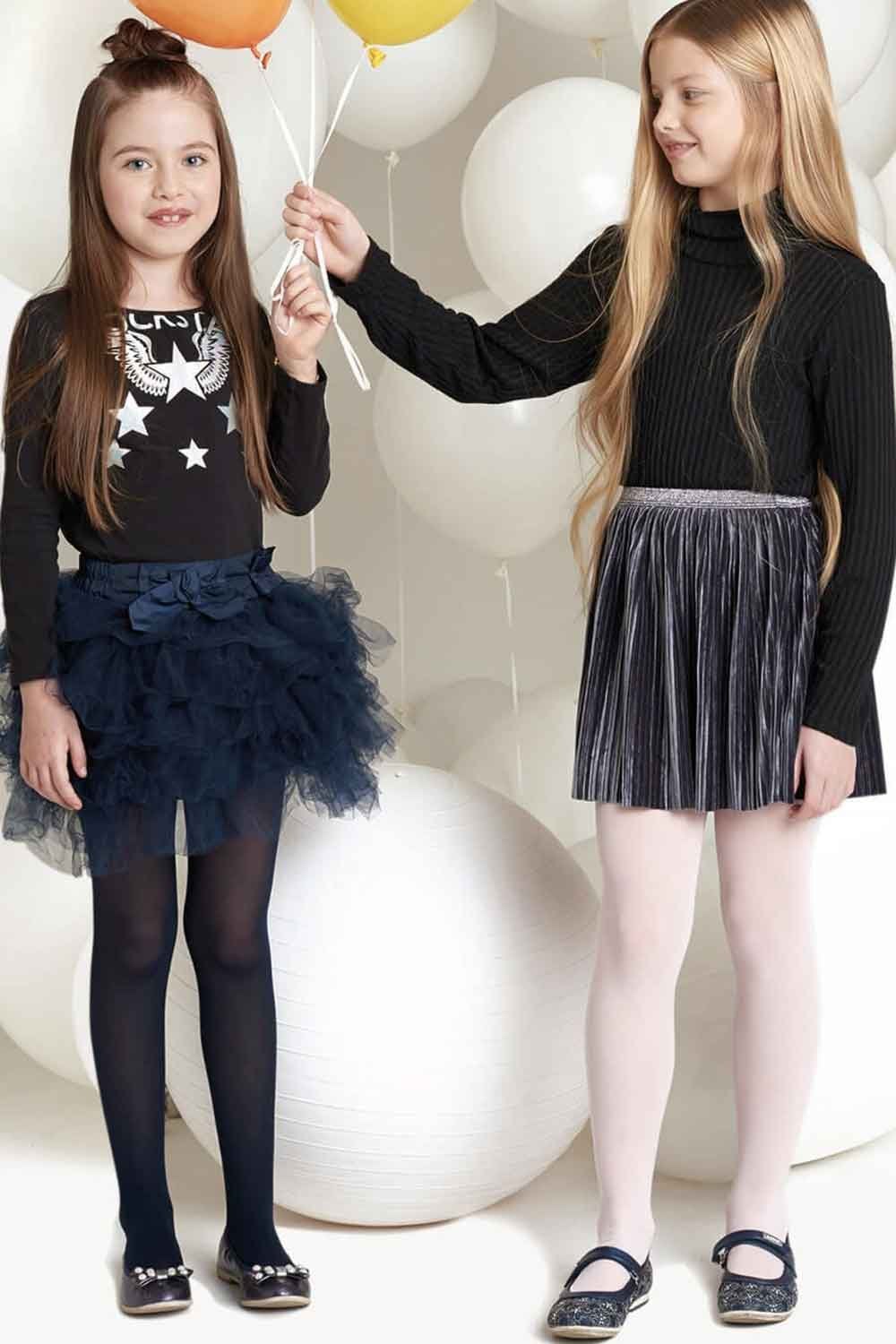Two young girls in stylish outfits and tights with balloons in the background