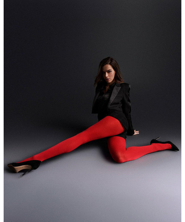 Woman wearing red falke tights and a black outfit sitting on a grey floor against a dark background