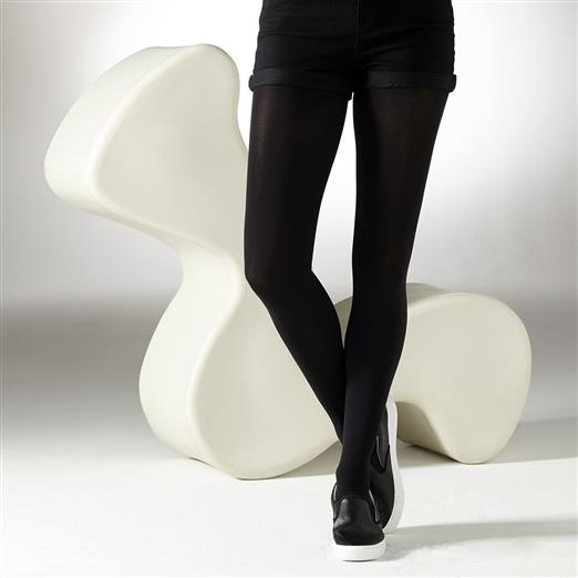 Model wearing black tights and shoes standing on a white surface with a modern white chair.