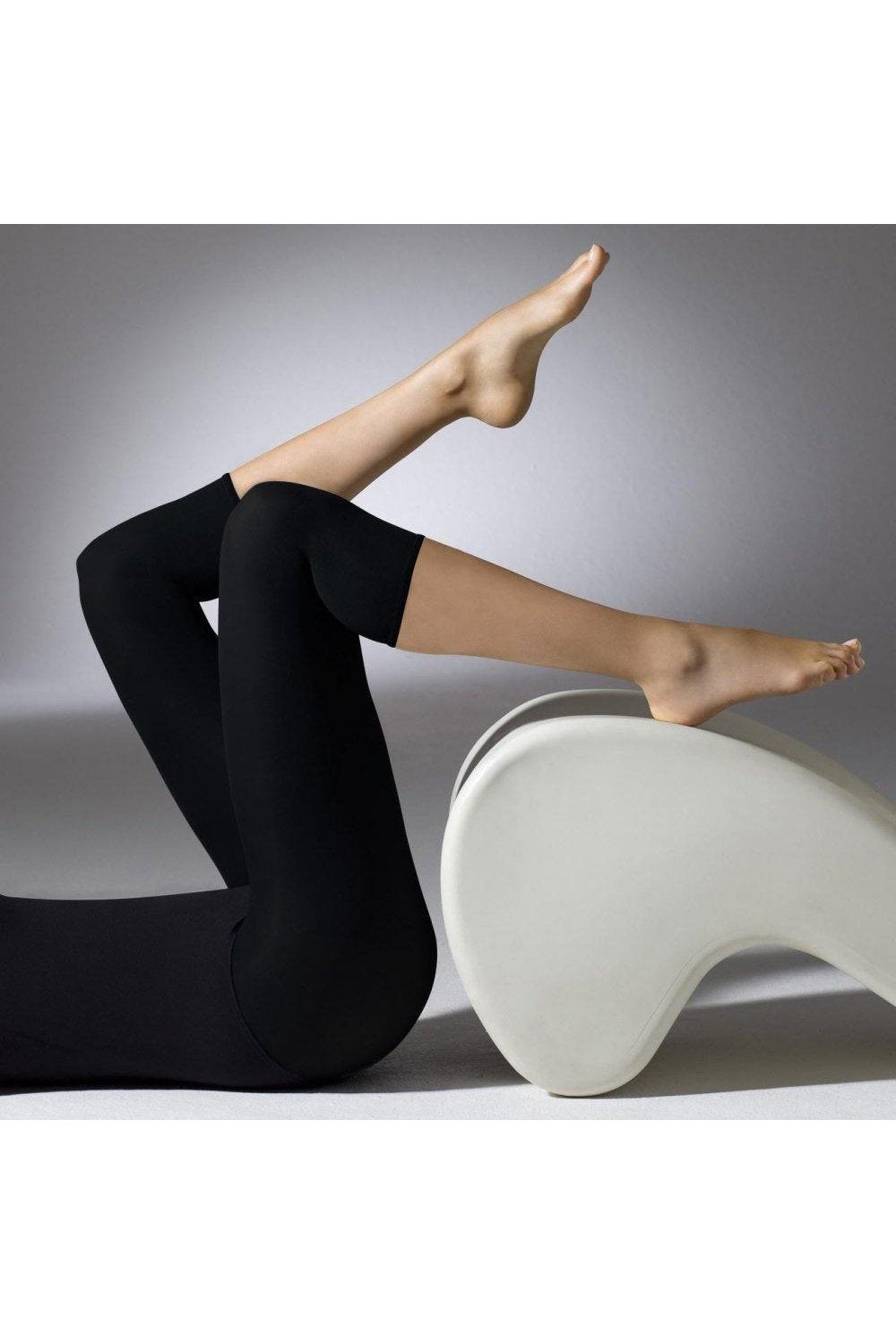 Model wearing black footless tights on a white chair against a gray background