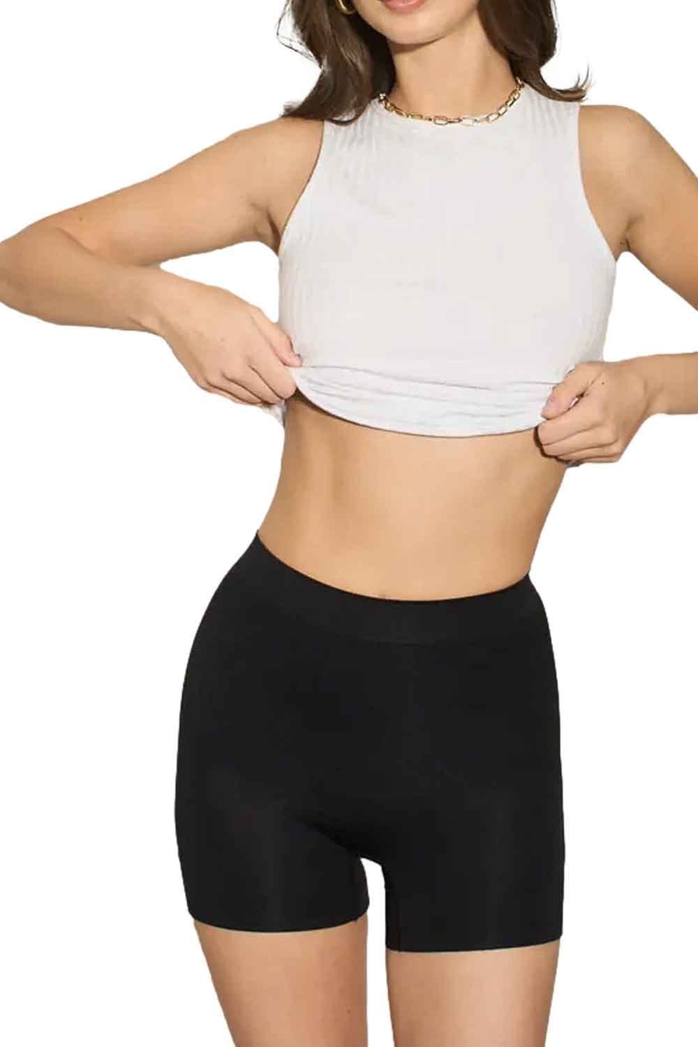 Model wearing a white crop top and black shapewear shorts on a white background
