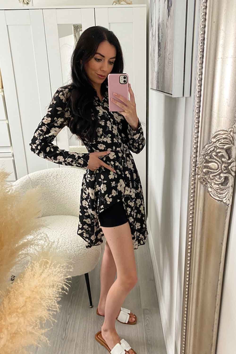 Model taking a mirror selfie wearing a floral dress and black shapewear  shorts in a room with decorative elements.