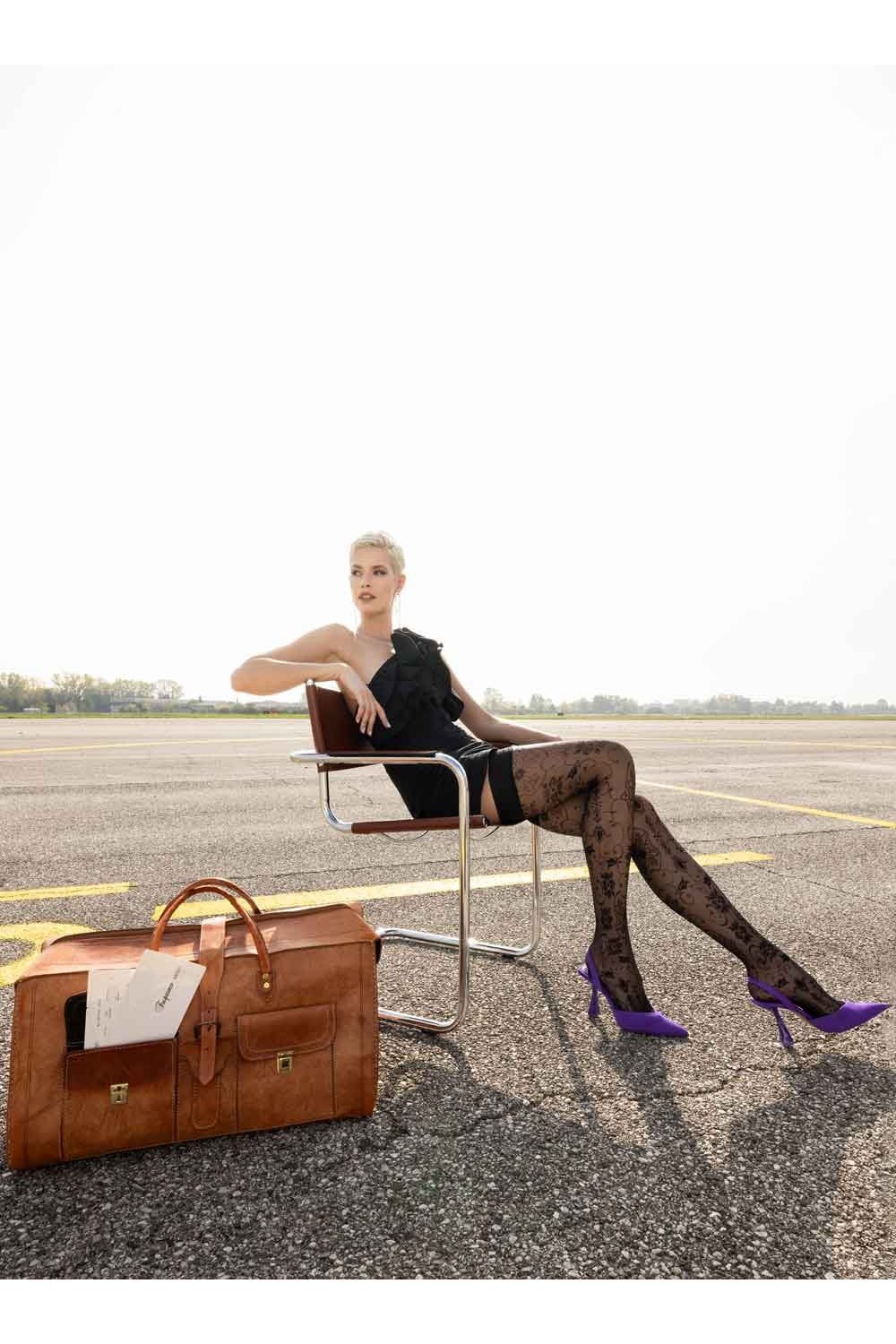 Woman sitting on a chair wearing floral patterned hold ups with a suitcase 