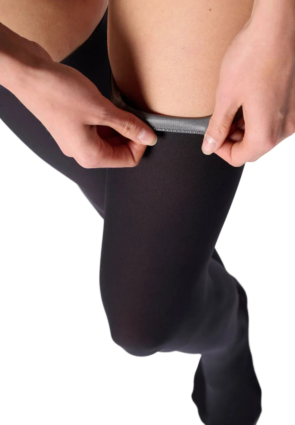 Close-up of a person wearing black hold ups and pulling up the top band with both hands against a white background.