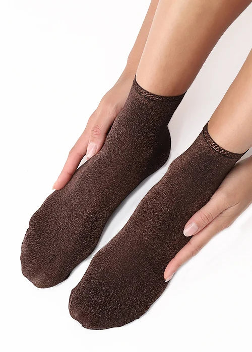 A pair of bronze ankle socks worn on a person's feet, with hands holding the sides of the socks to show their texture, against a plain white background.