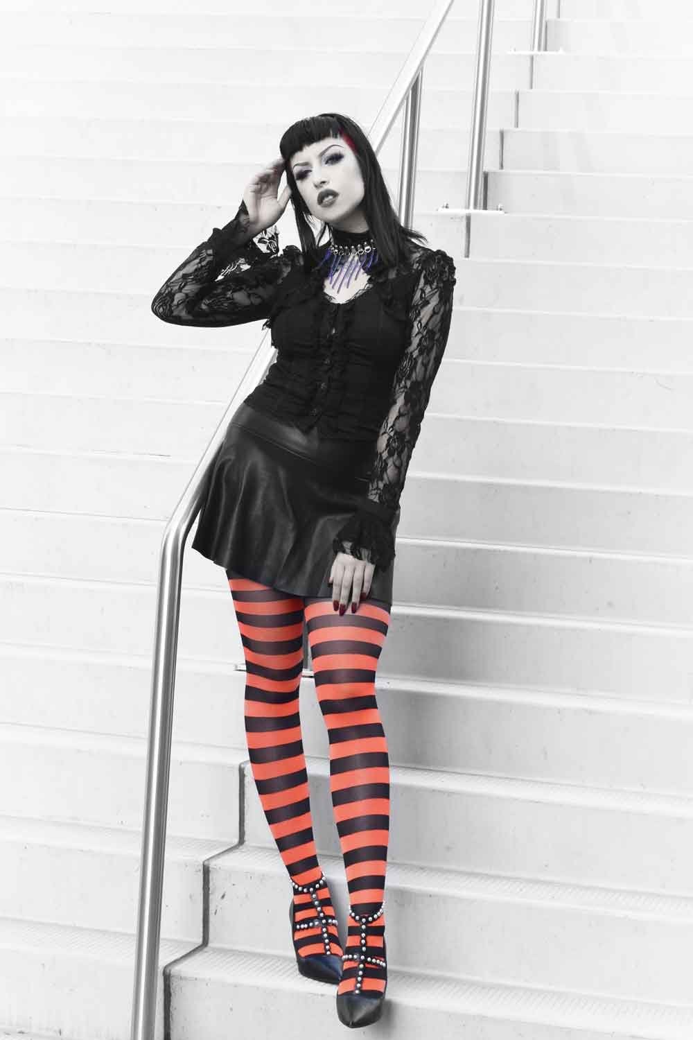 Person wearing a black outfit with red and black striped tights  on a white staircase.
