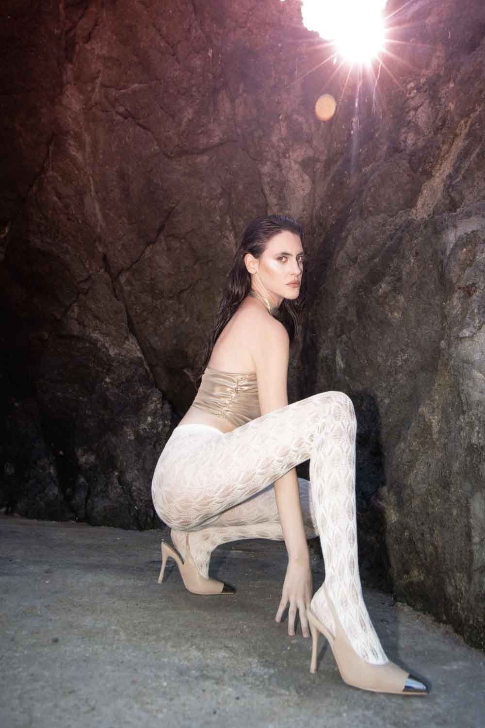 Woman wearing polaris white lace design tights posing against a rocky background