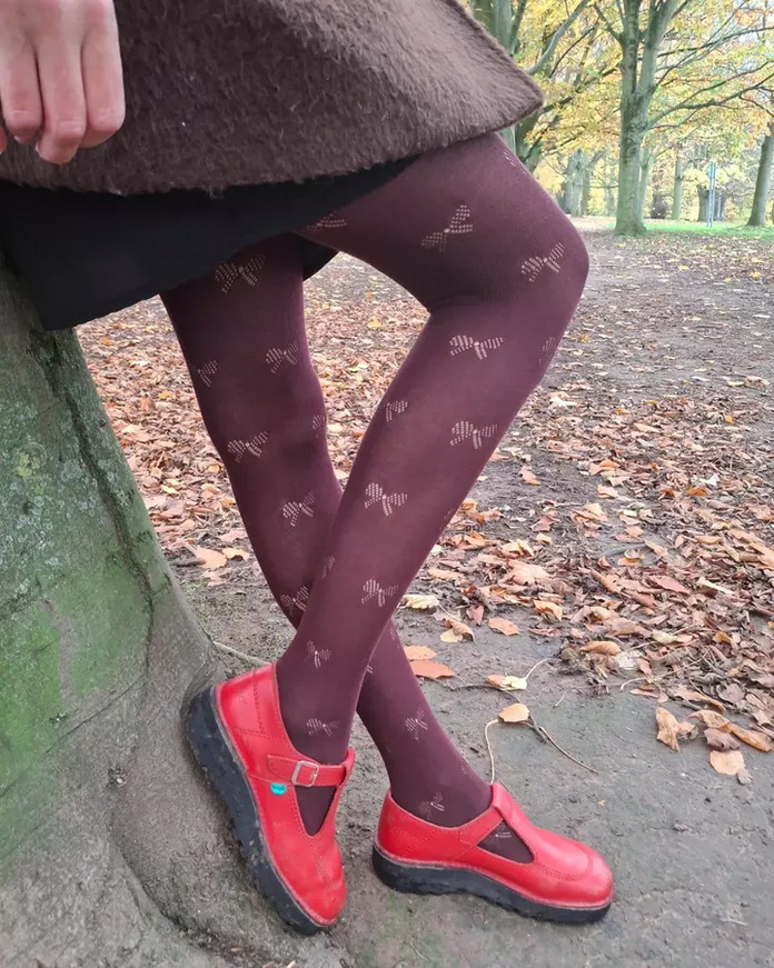 Person wearing burgundy tights with red shoes in a park setting.