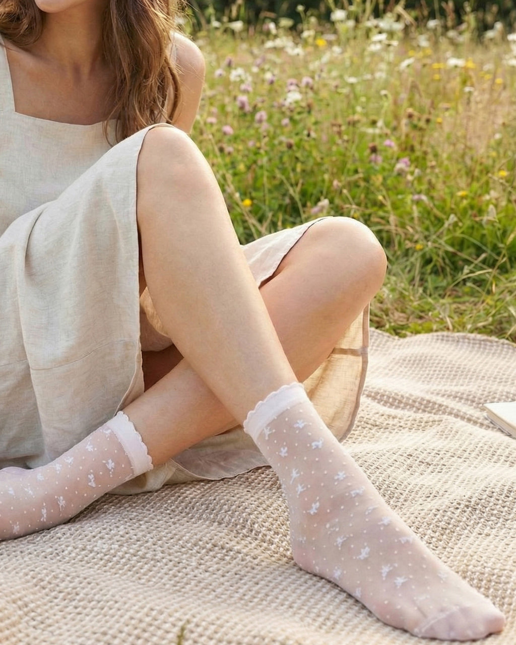 Woman sitting on a blanket in a field wearing sheer  white bow patterned socks