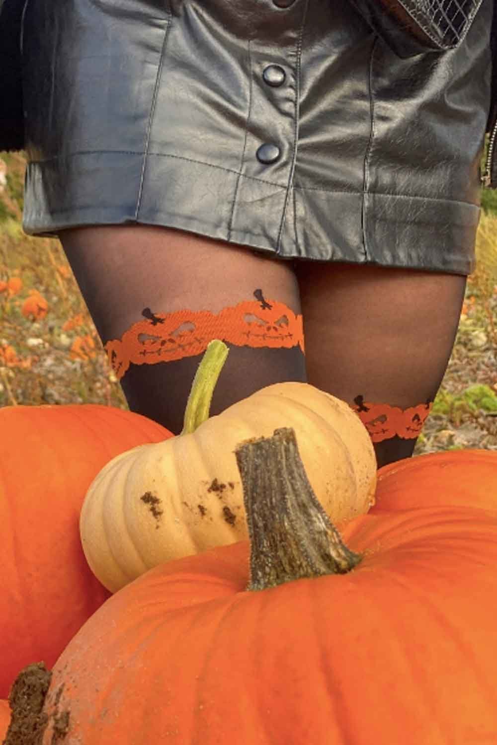 Person wearing over the knee pumpkin design tights  in front of pumpkins.