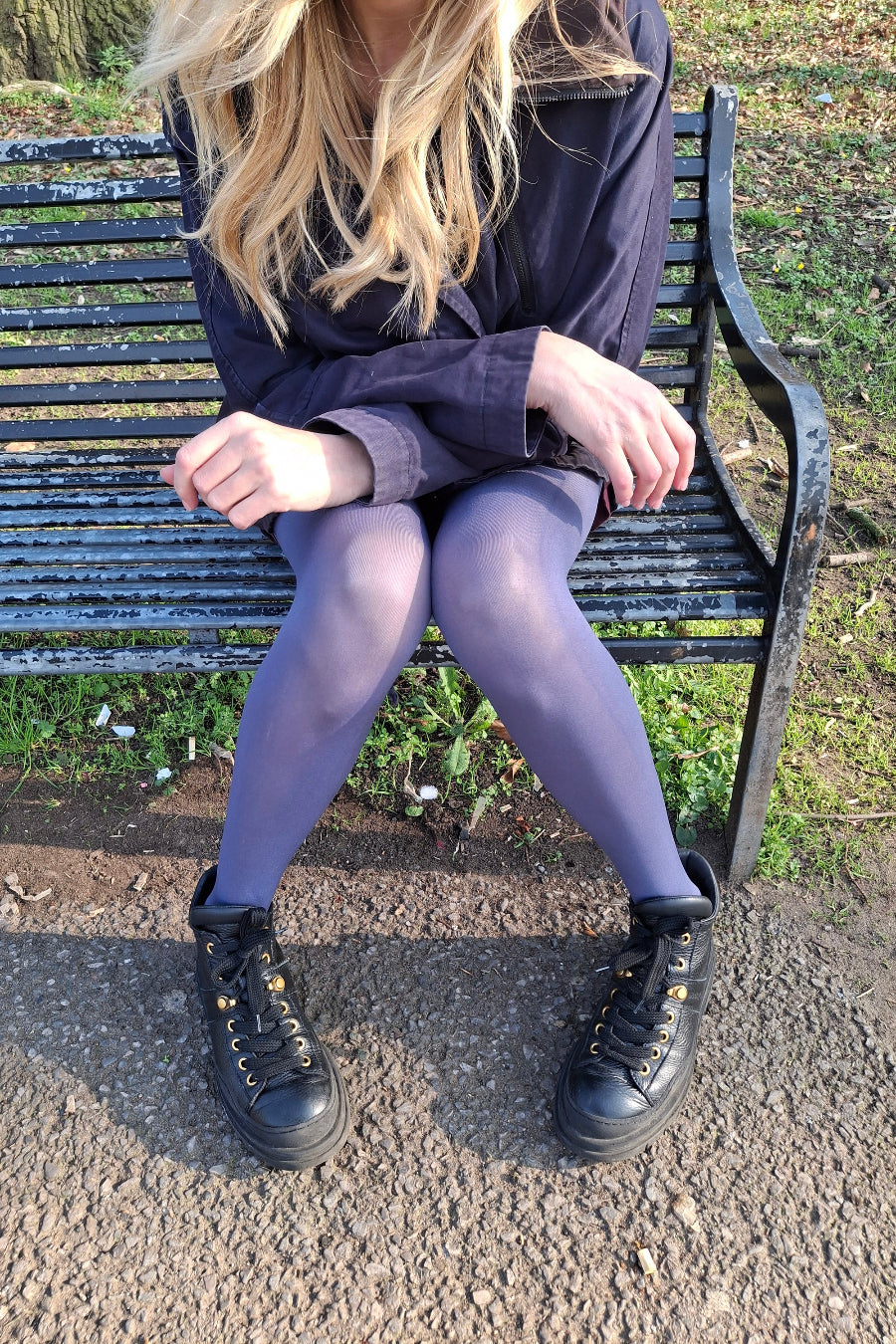Person sitting on a bench wearing a dark coat, tights, and black shoes.
