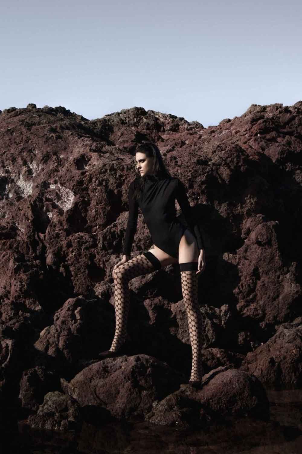 Person in black outfit and  Bellarix hold ups standing on rocky terrain