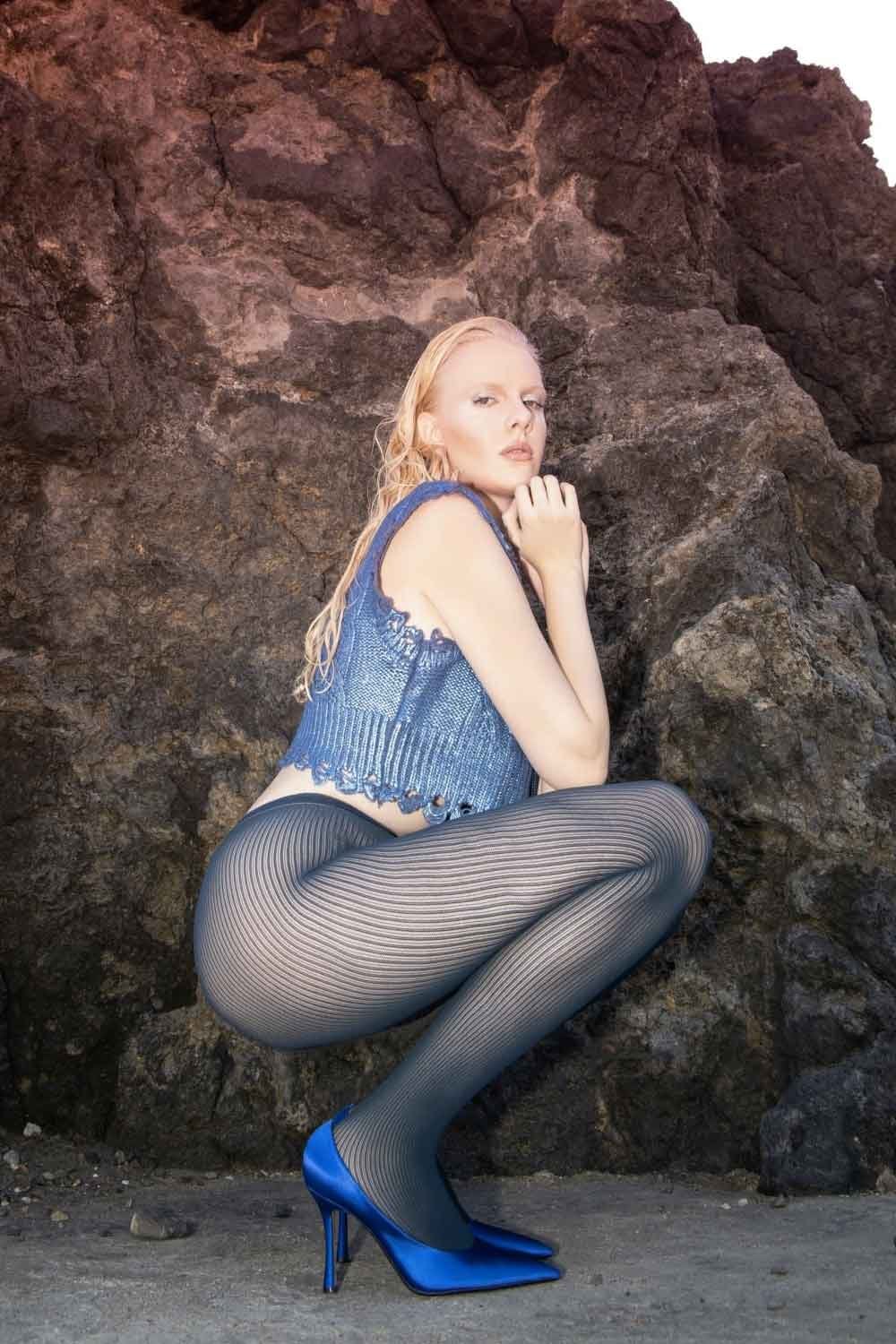 Woman in denim top and dubne ribbed tights sitting against a rocky background