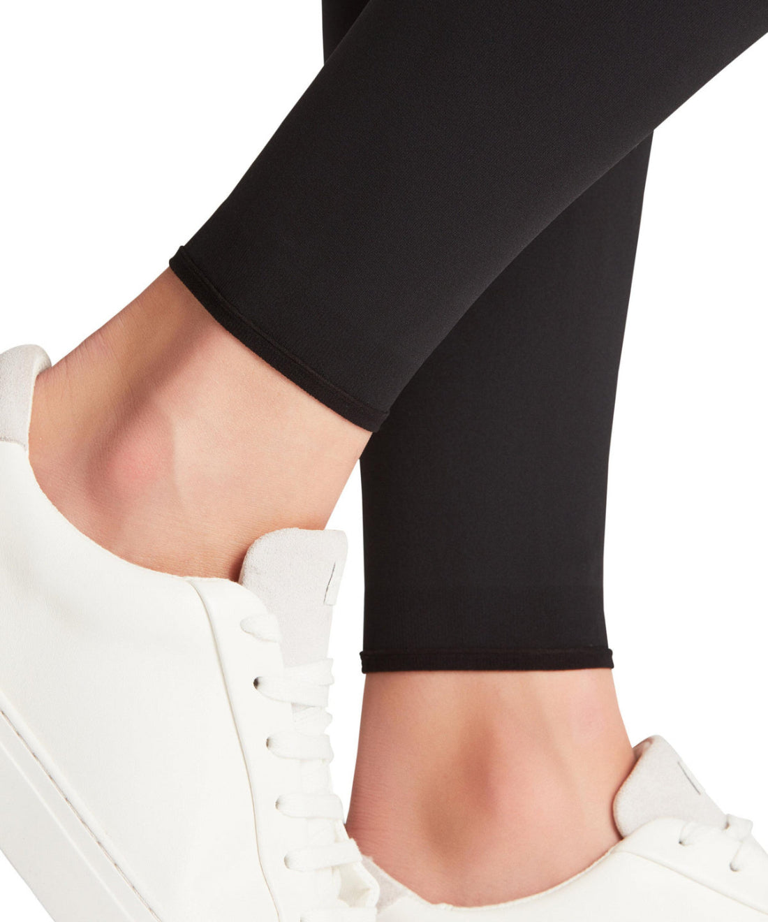 Black leggings worn with white sneakers on a white background
