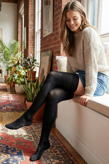 Woman wearing black hold ups sitting on a windowsill in a cosy room with plants.