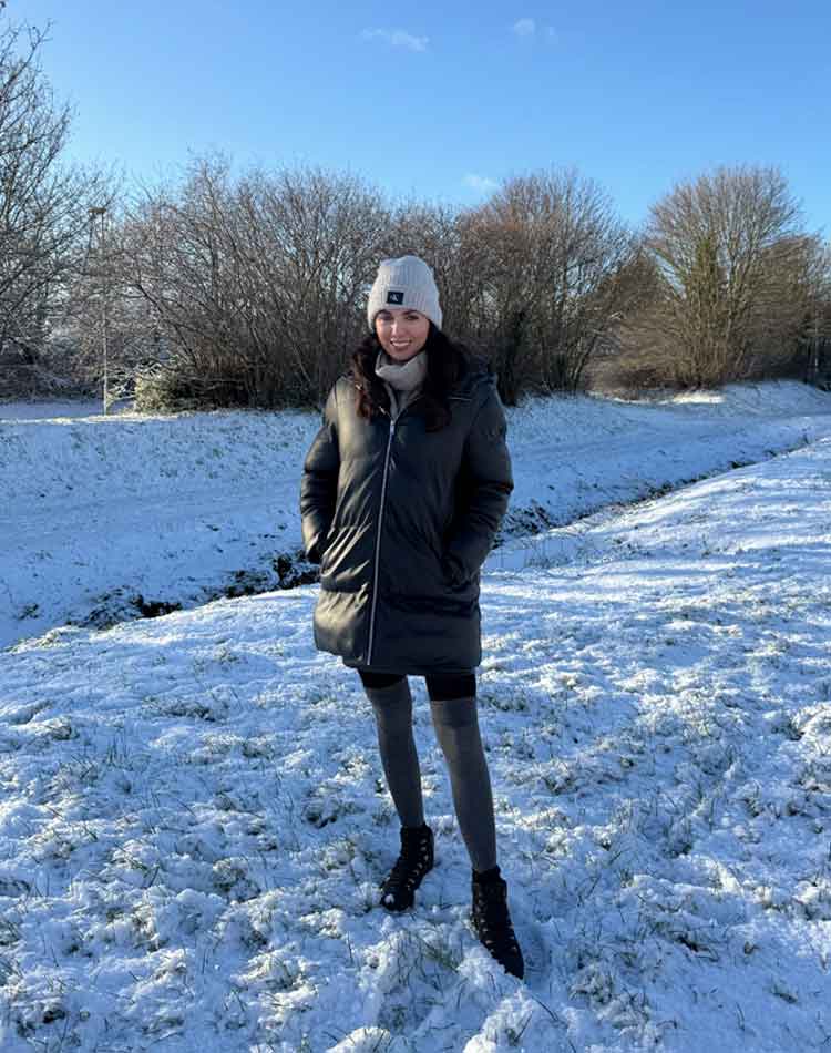 Person standing in a snowy landscape wearing winter clothing including opaque tights